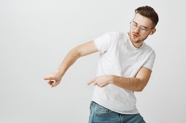 Homme heureux insouciant pointant vers la gauche comme danse dans des écouteurs sans fil, écoute de la musique