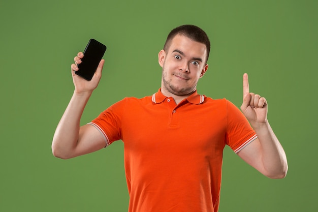 L'homme heureux montrant à l'écran vide du téléphone mobile contre le mur vert.
