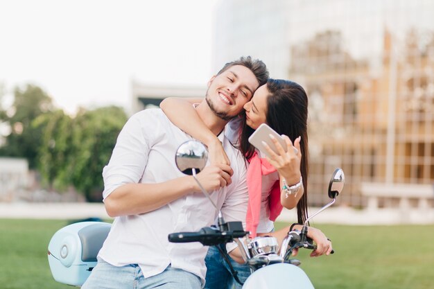 Homme heureux posant sur scooter pendant que son ami l'embrasse