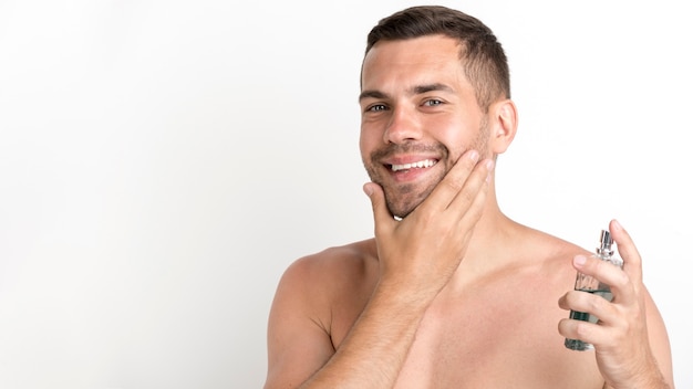 Homme heureux, pulvérisation de lotion après-rasage, debout sur fond blanc