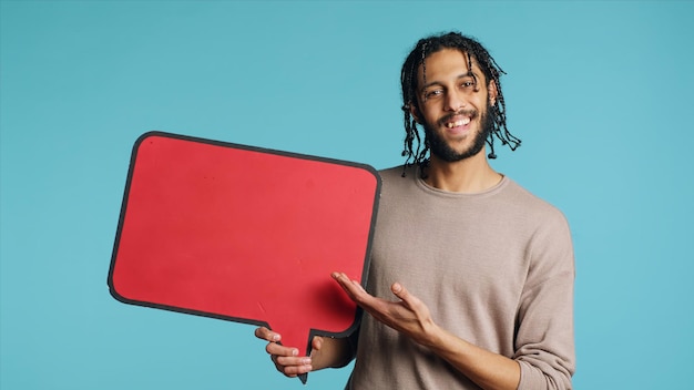 Homme heureux tenant un discours rouge avec un panneau de bulle à l'arrière-plan du studio