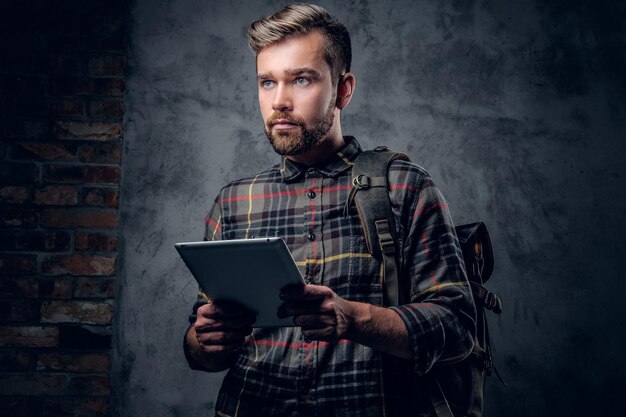 Homme hipster barbu en chemise polaire tient une tablette PC sur fond gris.