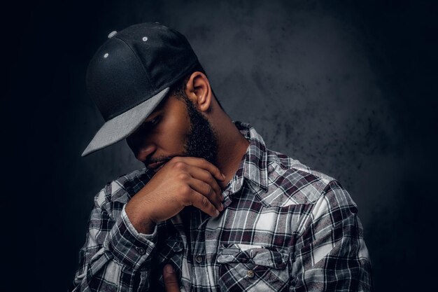 Homme hipster noir et barbu réfléchi vêtu d'une chemise polaire et d'une casquette de baseball.