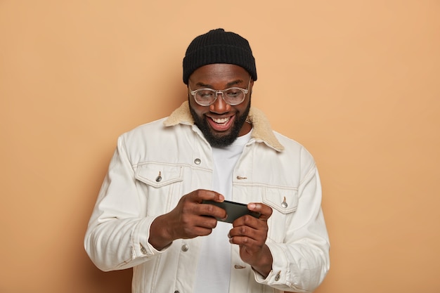 Homme hipster noir avec expression positive joue à des jeux vidéo