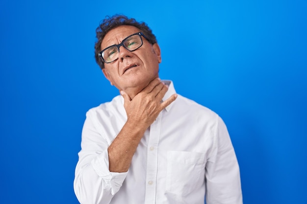 Photo gratuite homme hispanique d'âge moyen debout sur fond bleu touchant le cou douloureux mal de gorge pour la grippe et l'infection