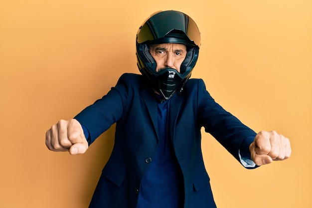 Homme hispanique d'âge moyen portant un casque de moto faisant le symbole de la moto avec les mains gonflant les joues avec un visage drôle. bouche gonflée d'air, captant l'air.