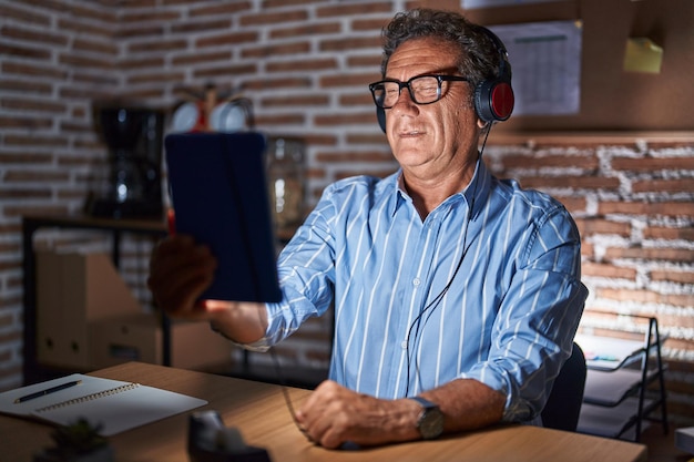 Photo gratuite homme hispanique d'âge moyen utilisant un pavé tactile assis sur la table la nuit en regardant la caméra avec une expression sexy, un visage joyeux et heureux.