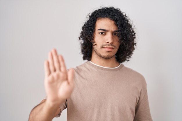 Photo gratuite homme hispanique aux cheveux bouclés debout sur fond blanc arrêtant de chanter avec la paume de la main expression d'avertissement avec un geste négatif et sérieux sur le visage