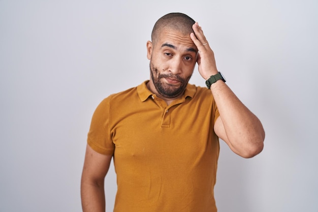 Homme hispanique avec barbe debout sur fond blanc inquiet et stressé par un problème avec la main sur le front, nerveux et anxieux de crise