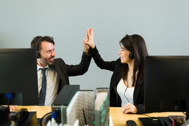 Un homme hispanique et une jeune femme avec un casque faisant un high five tout en travaillant ensemble dans un centre d'appels. Représentant commercial célébrant une vente d'entreprise