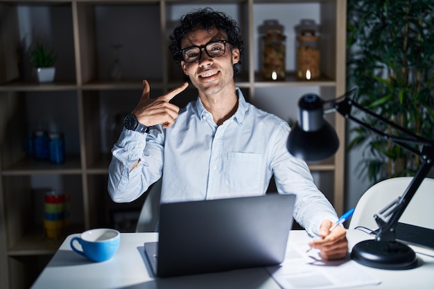 Photo gratuite homme hispanique travaillant au bureau la nuit souriant joyeux montrant et pointant avec les doigts les dents et la bouche concept de santé dentaire