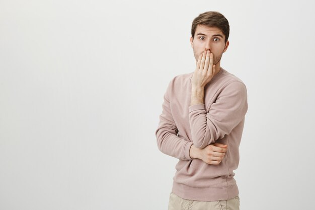 Homme impressionné choqué haletant et couvrant la bouche, fixant