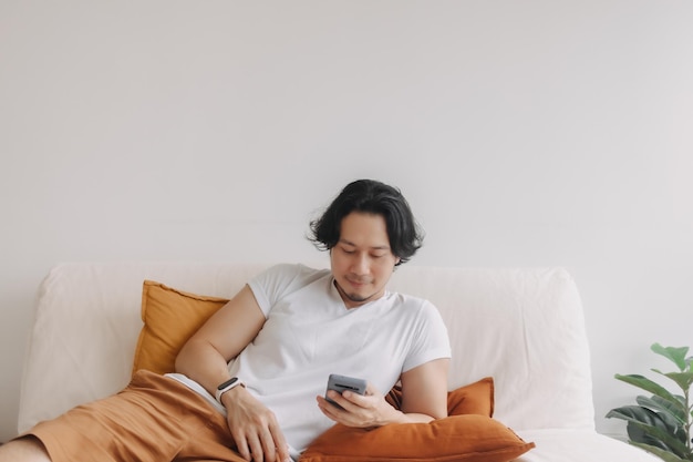 Un homme indépendant aux cheveux longs s'assoit sur le canapé et utilise un smartphone d'application