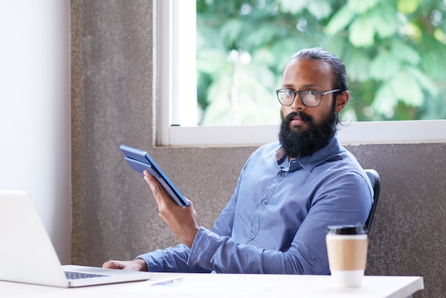 Homme indien assis au bureau au bureau et à l'aide d'une tablette