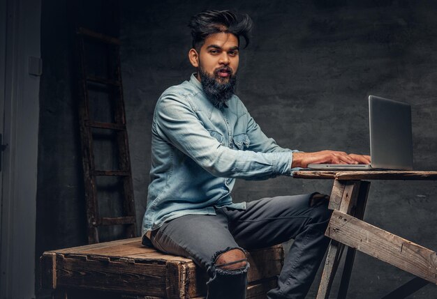 Homme indien barbu élégant travaillant avec un ordinateur portable.