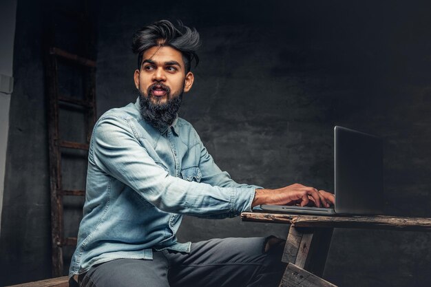 Homme indien barbu élégant travaillant avec un ordinateur portable.