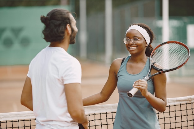 Homme indien et femme noire américaine debout sur un court de tennis