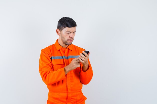 Homme industriel à l'aide de téléphone portable en uniforme et à la vue de face, occupé.