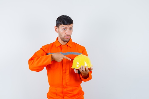 Homme industriel pointant sur casque en uniforme, vue de face.