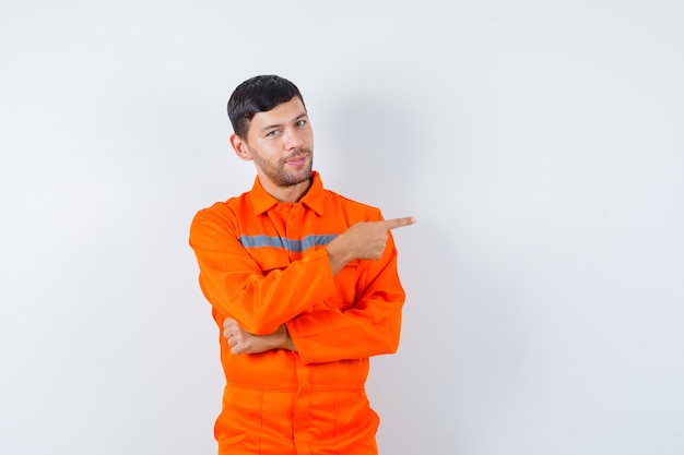 Homme industriel pointant vers le côté en uniforme et à la joyeuse. vue de face.