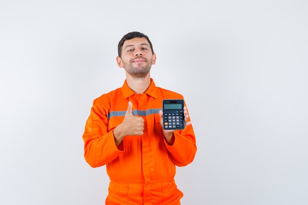 Homme industriel tenant la calculatrice, montrant le pouce vers le haut en uniforme et à la recherche de joie. vue de face.