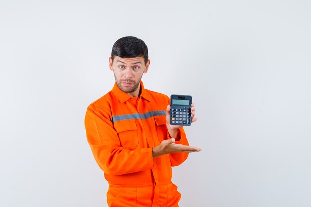 Homme industriel en uniforme montrant la calculatrice et l'air confiant, vue de face.