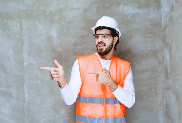 Homme ingénieur en casque blanc et lunettes de protection pointant sur son collègue ou sur quelque chose de côté.