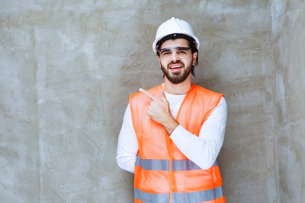 Homme ingénieur en casque blanc et lunettes de protection pointant sur son collègue ou sur quelque chose de côté.