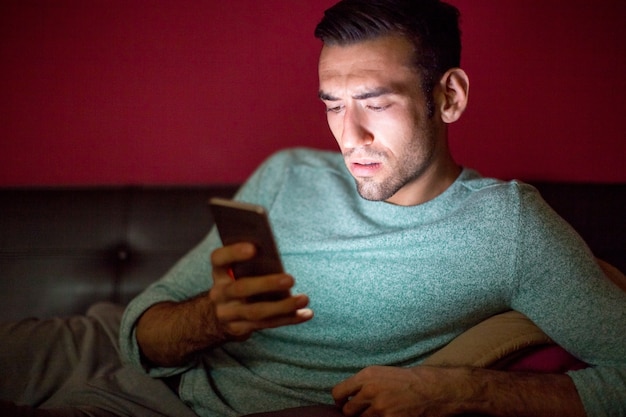 Homme inquiet à l&#39;aide d&#39;un téléphone intelligent sur le canapé à la nuit