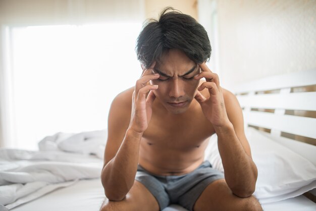 Homme inquiet assis sur un lit le matin, sérieux, pensant à quelque chose