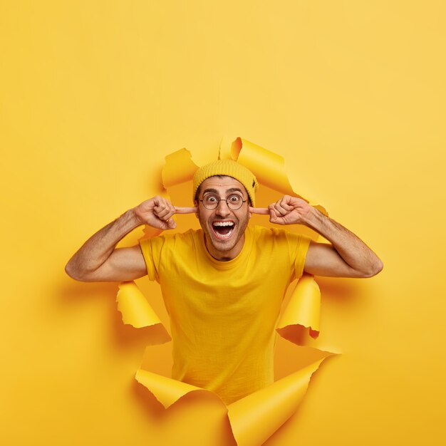 Un homme insouciant avec une expression joyeuse bouche les trous d'oreille, sourit à la caméra