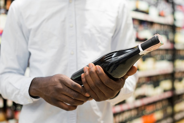 Homme inspectant une bouteille de vin dans une section alcool