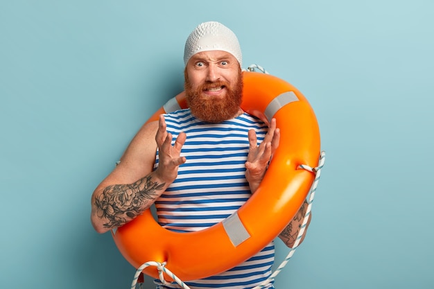 Homme irrité avec une barbe épaisse rouge, des gestes avec agacement, porte un bonnet en caoutchouc