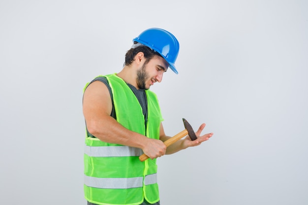 Homme Jeune Constructeur Frappant Le Marteau Sur La Paume En Uniforme De Vêtements De Travail Et à La Joyeuse Vue De Face.