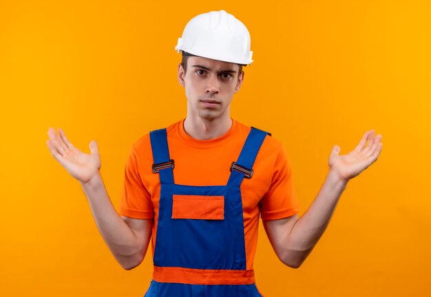 Homme jeune constructeur portant un uniforme de construction et un casque de sécurité confus