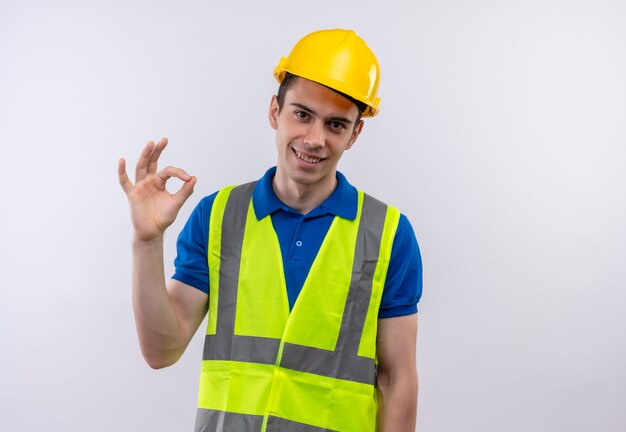 Homme jeune constructeur portant l'uniforme de construction et un casque de sécurité faisant ok avec les doigts