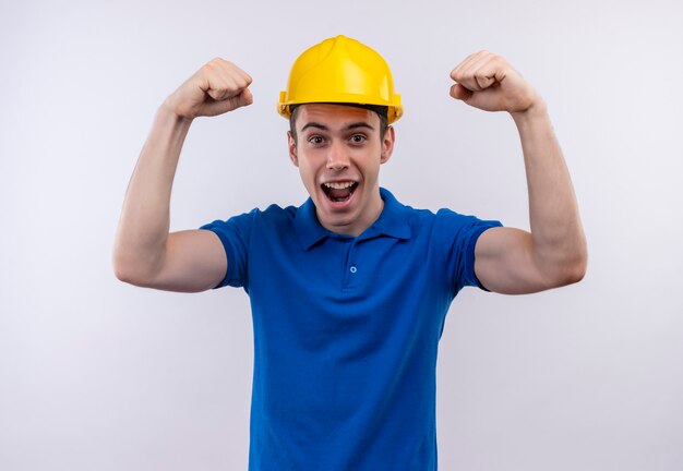 Homme jeune constructeur portant l'uniforme de construction et un casque de sécurité faisant des poings heureux