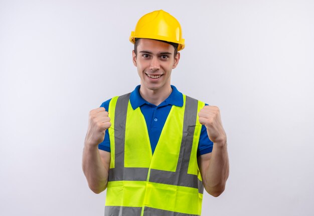Homme jeune constructeur portant l'uniforme de construction et un casque de sécurité montre joyeusement la puissance avec les poings