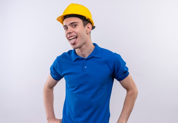 Homme jeune constructeur portant l'uniforme de construction et un casque de sécurité montre la langue