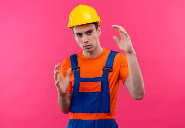 Homme jeune constructeur portant l'uniforme de construction et un casque de sécurité montre la taille avec les mains