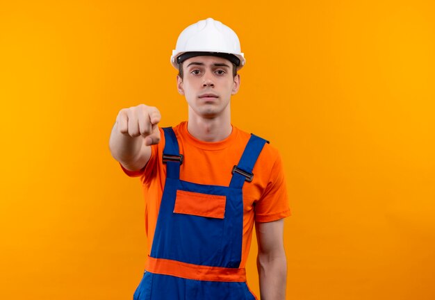 Homme jeune constructeur portant un uniforme de construction et un casque de sécurité pointe le doigt