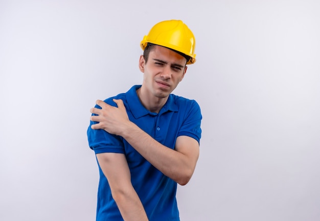 Homme jeune constructeur portant des uniformes de construction et un casque de sécurité faisant face malheureuse et souffre de douleur