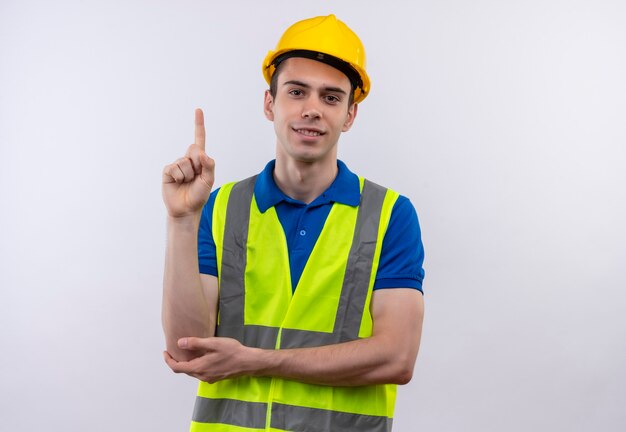 Homme jeune constructeur portant des uniformes de construction et un casque de sécurité pointe vers le haut