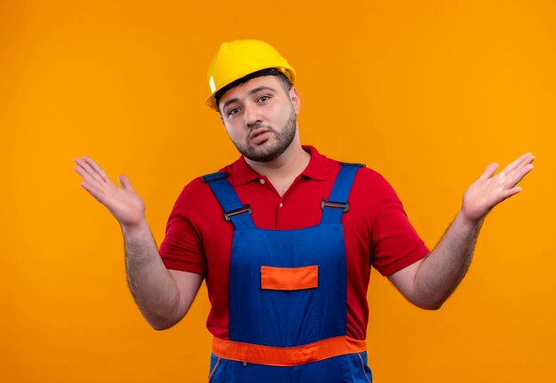 Homme jeune constructeur en uniforme de construction et casque de sécurité à la confusion des bras sur les côtés