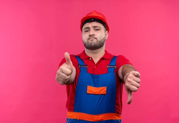 Homme jeune constructeur en uniforme de construction et casque de sécurité montrant des coups de haut en bas à la confusion