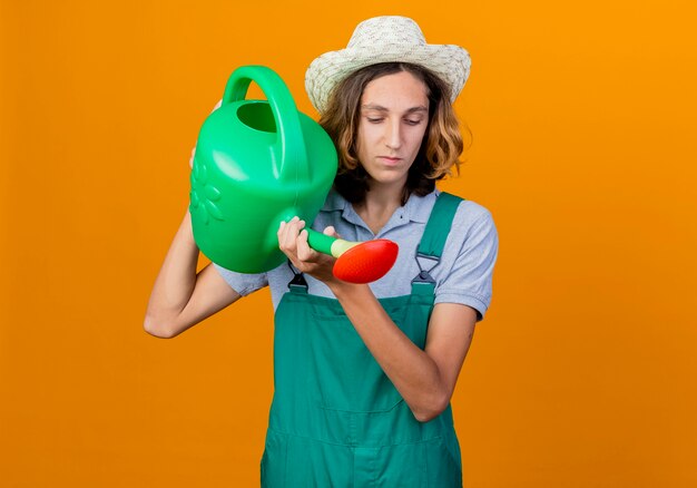 Homme jeune jardinier portant combinaison et chapeau tenant un arrosoir