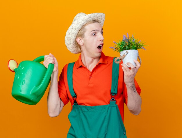 Homme jeune jardinier portant combinaison et chapeau tenant un arrosoir