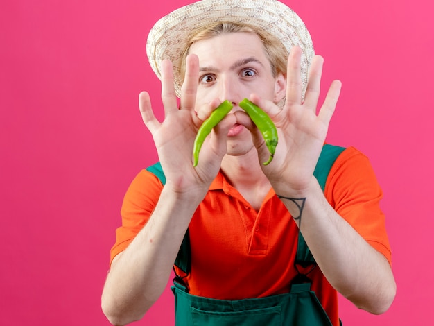 Homme jeune jardinier portant combinaison et chapeau tenant les moitiés de piment vert