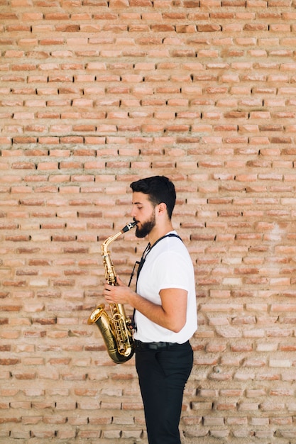 Photo gratuite homme jouant du sax avec fond de mur de brique