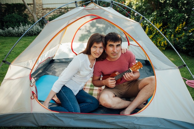 Homme jouant du ukulélé assis avec sa femme dans une tente en regardant la caméra